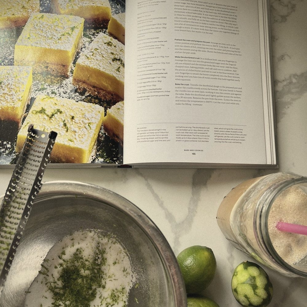 An open cookbook beside a bowl of lime-zested sugar, mid-test